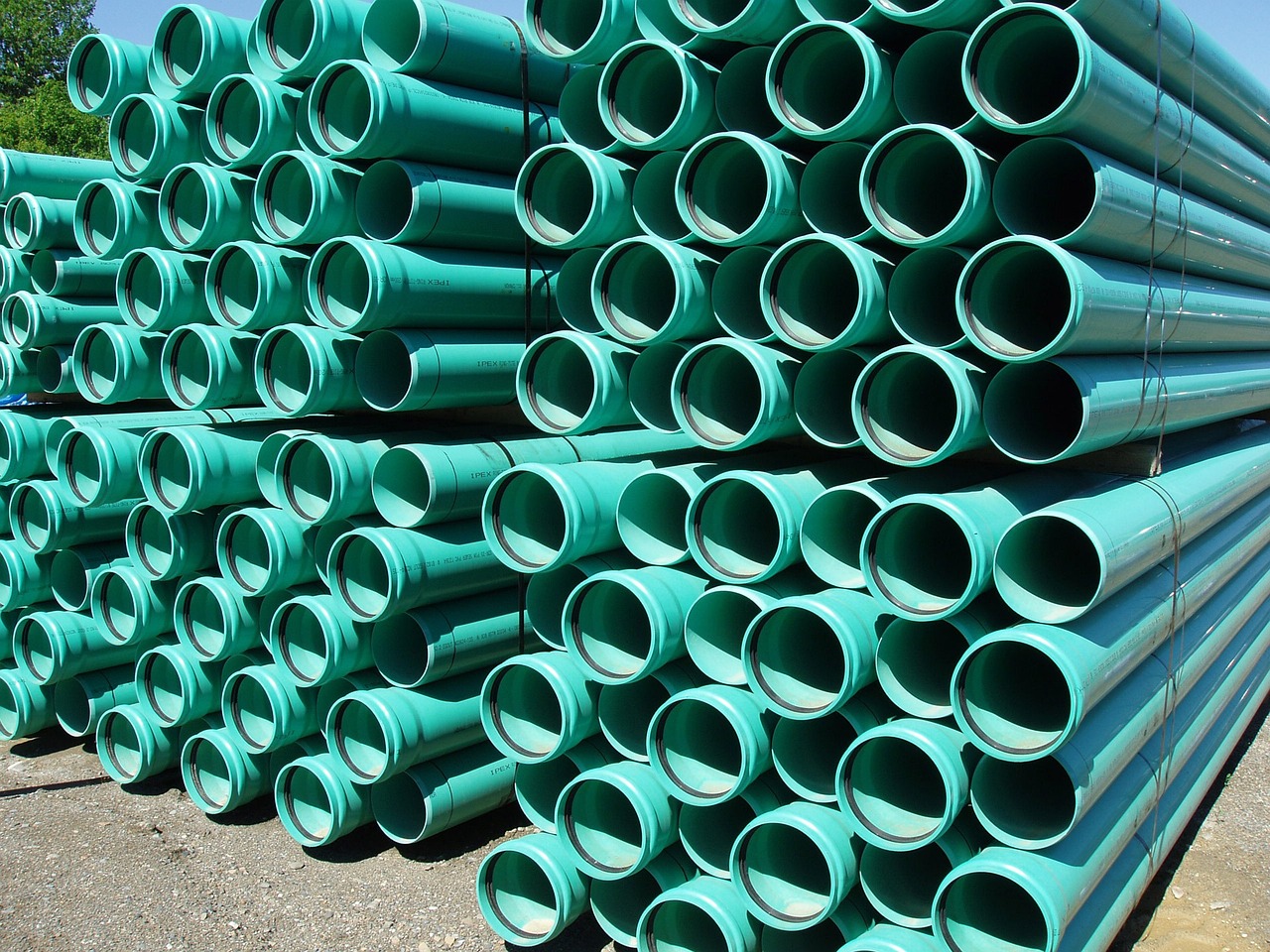 Stack of green plastic pipes bundled outdoors on gravel surface.
