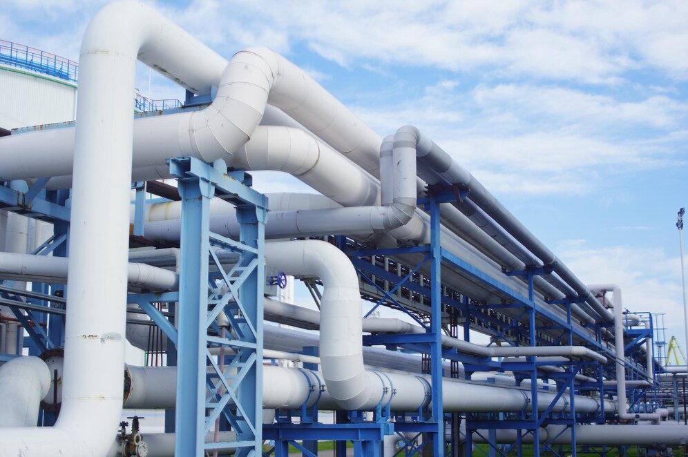 Large industrial white pipelines supported by blue steel structures at a processing facility