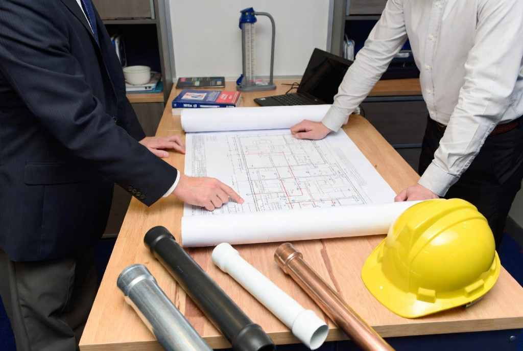 Fire sprinkler system planning consultation with pipe material samples and blueprints for material selection